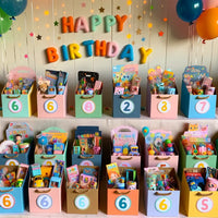Eine -Ausstellung- von- personalisierten -Partygeschenk-Boxen- für -eine- Geburtstagsfeier -für- 6-Jährige, jede -Box- ist -mit -dem -Namen -des- Kindes- dekoriert -und -gefüllt- mit -altersgerechten -Spielzeugen- und -Leckereien.